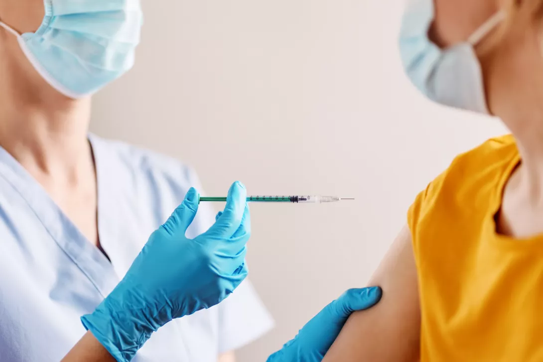 Masked health care worker administers a vaccine shot.